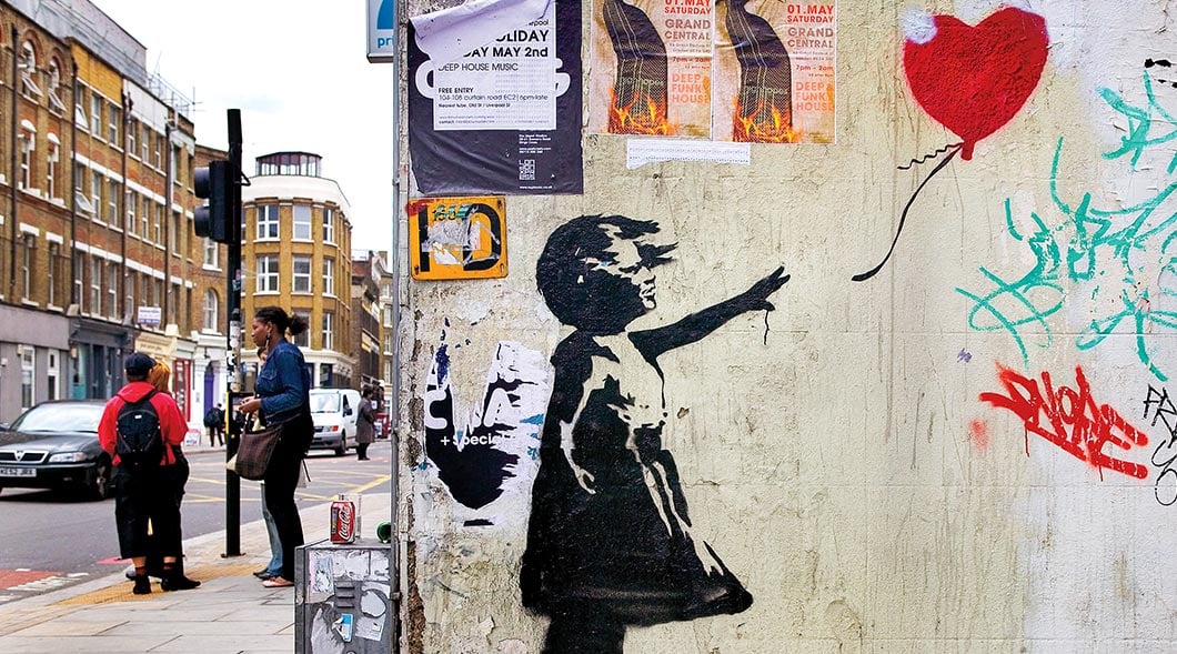 Banksy's Girl With Balloon mural on a London street corner with two people nearby